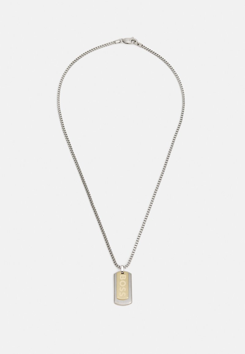 Collar de cadena de plata con un colgante rectangular que presenta una inscripción "BOSS" en tono dorado. Textura suave, diseño minimalista.