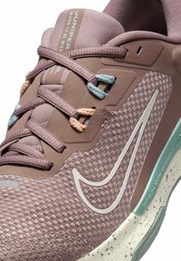 Ljubičaste atletske tenisice s teksturiranim gornjim dijelom, kontrastnim svijetloplavim i breskvastim vezicama, bijelim Nike logotipom i točkom detaljima na potplatu.