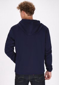 Felpa blu navy vista da dietro, con cappuccio regolabile e maniche lunghe, realizzata in tessuto liscio e morbido. Jeans scuri visibili sotto.
