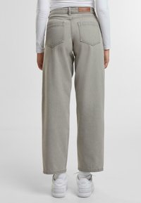 Jeans de pierna ancha gris claro hechos de mezcla de algodón, con dos bolsillos traseros y un parche de cuero marrón de la marca en la cintura. Par de zapatillas blancas.