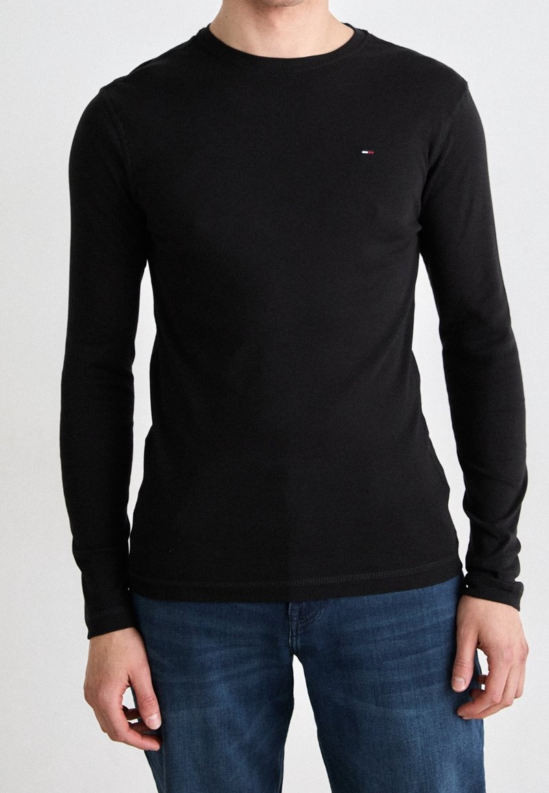 Zwart langemouwen shirt met een ronde hals en subtiele logo-accent, gemaakt van een gladde stof, gecombineerd met blauwe spijkerbroeken.