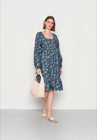 Vestido floral com decote quadrado, cintura franzida e mangas longas e bufantes em azul marinho, com padrões florais verdes e rosas. Inclui uma bolsa bege.