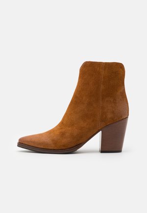 Botín de ante marrón hasta el tobillo con punta afilada, tacón de madera de altura media y un diseño aerodinámico. Textura suave con un acabado limpio.