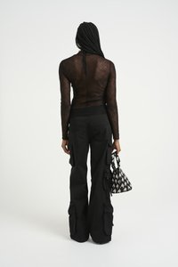Top lungo a maniche nere trasparenti con texture intricata; abbinato a pantaloni neri larghi con tasche cargo; tiene una borsa a tracolla con motivo.