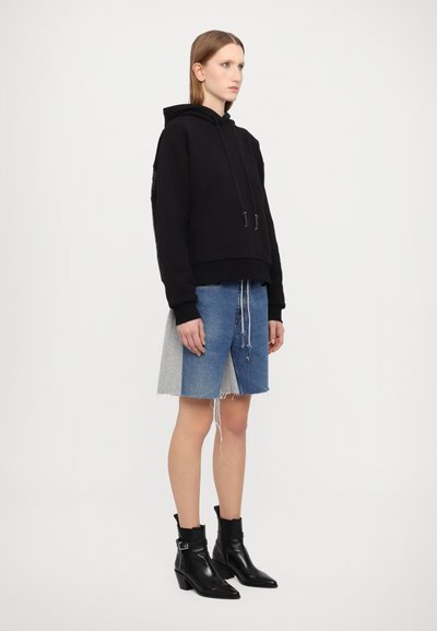 Hanorac negru cu glugă și șnururi, asortat cu o fustă din denim în două tonuri (albastru și gri) și cizme negre ankle cu toc pătrat.