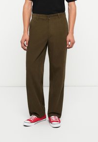 Bruine ribfluwelen broek met een recht, gesneden ontwerp, voorzien van een knoopsluiting en discrete zijzakken, gecombineerd met rode sneakers.
