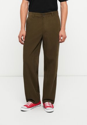 Pantaloni in cotone color marrone con design a gamba dritta, dotati di chiusura a bottone e tasche laterali discrete, abbinati a sneakers rosse.