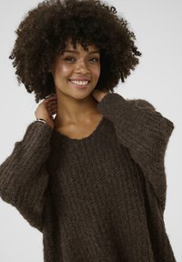 Brown textured sweater with a loose fit, wide sleeves, and a scoop neckline. The material appears soft and cozy, suitable for casual wear.