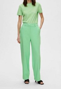 T-shirt verde menta e pantaloni larghi coordinati, con una texture liscia e una vestibilità su misura. Indossati con sandali neri con tacco.