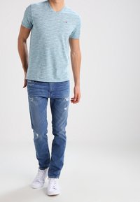 Ljusblå v-ringad t-shirt med subtil textur, kombinerad med medelblå jeans med slitna detaljer och vita sneakers.