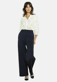 Blusa blanca con textura estampada, botones delanteros y mangas tres cuartos combinada con pantalones de pierna ancha azul marino de talle alto y zapatos planos bicolor.