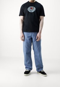 Zwart T-shirt met een afbeelding van een flesdop, blauwe broek met rechte pijpen, en zwarte sneakers met witte veters. Eenvoudig ontwerp en een ontspannen pasvorm.