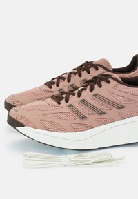Baskets de sport en maille rose pâle avec des accents et des lacets marron foncé, dotées d'une semelle blanche rembourrée et de motifs texturés sur le dessus.