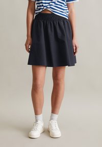 Zwarte rok met een elastische tailleband, A-lijn silhouet, gladde textuur en knielange afwerking, gedragen met witte sneakers en sokken.