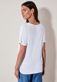T-shirt blanc, ample, avec des manches courtes retroussées et une délicate couture verticale à l'arrière. Tissu doux et texturé avec une coupe décontractée.