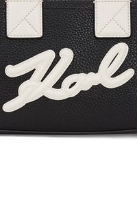 Black textured leather bag featuring a white, raised "Karl" logo. Includes two white accents at the top. Compartment with zip closure.