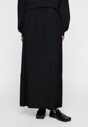 Gonna maxi nera realizzata in tessuto morbido, con vita regolabile e dettagli sulle cuciture laterali. Abbinata a mocassini neri lucidi.