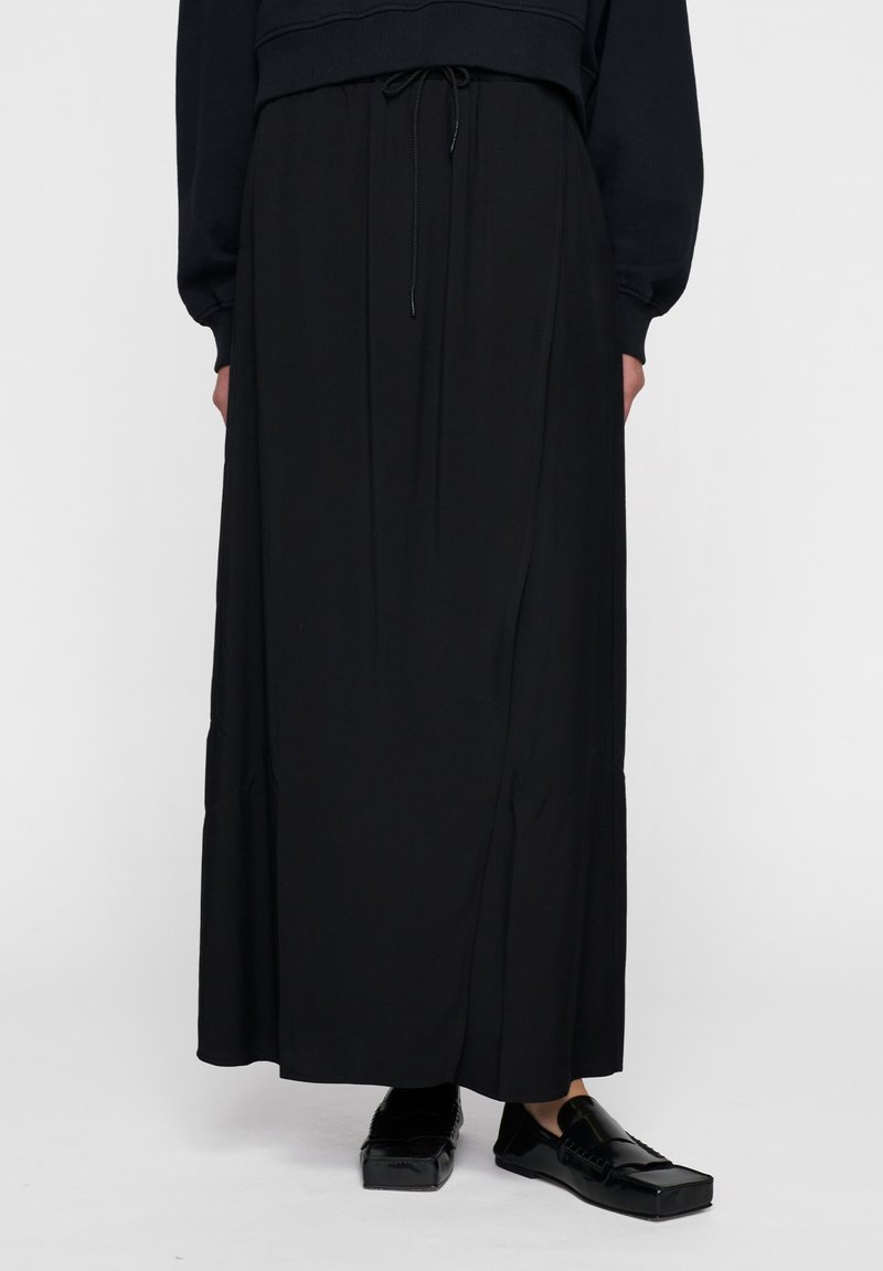 Zwarte maxi rok van zachte stof, met een tailleband met trekkoord en zijnaaddetails. Gepaard met glanzende zwarte loafers.