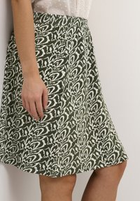 Jupe verte avec un motif abstrait blanc, de longueur intermédiaire, dotée d'une taille élastique et d'une forme fluide. Texture de tissu lisse.