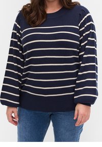 Námořnický modrý svetr vyrobený z měkké pleteniny, s širokými krémovými pruhy, kulatým výstřihem a objemovými rukávy; v kombinaci s modrými džínami.