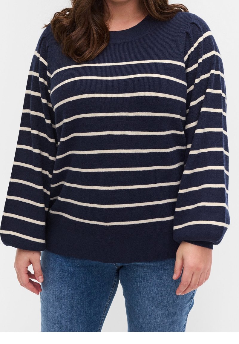 Námořnický modrý svetr vyrobený z měkké pleteniny, s širokými krémovými pruhy, kulatým výstřihem a objemovými rukávy; v kombinaci s modrými džínami.