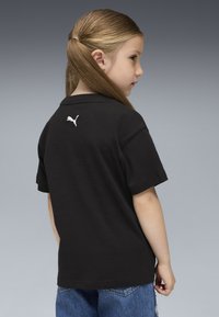 Melna kokvilnas polo krekls ar īsām piedurknēm, aizmugurē ar balto Puma logotipu. Valkāts ar zilām džinsām, ar vienkāršu, ikdienišķu dizainu.