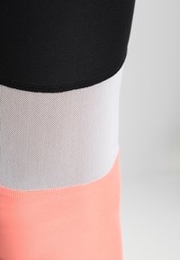 Leggings colorés avec une section supérieure noire, un panneau en maille blanche et une section inférieure rose. Le tissu est lisse avec un design ajusté.