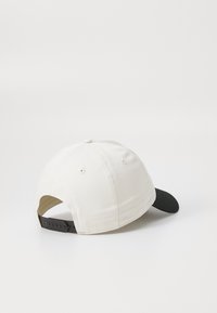 Cappello di cotone bianco con visiera nera, caratterizzato da una tesa curva, fori di ventilazione e una strap nera regolabile sul retro.