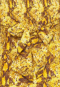 Gul och brun orm-mönstrad tyg med en strukturerad yta. Har en rosettdetalj vid midjan, vilket skapar ett samlat och lager-på-lager utseende.