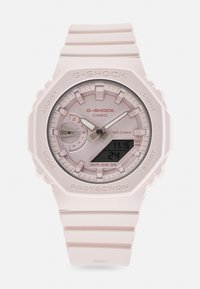 G-SHOCK óra világos rózsaszín műanyag pánttal, kerek számlappal és analóg-digitális kijelzővel. Jellemzői közé tartozik egy textúrázott keret és különböző gombok.