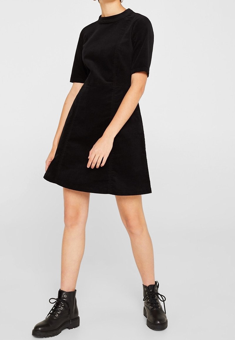 Schwarzes Cordkleid mit kurzen Ärmeln, Rundhalsausschnitt und A-Linien-Silhouette, kombiniert mit schwarzen Schnür-Stiefeletten.