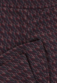 Donkere stof met een abstract zigzagpatroon in gedempte roze en dieprode tinten, met een zichtbaar gevouwen naaddetail.