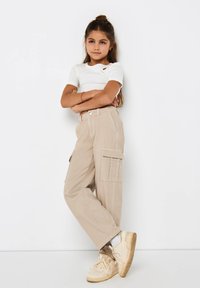 Top corto bianco a maniche corte con un piccolo taglio, abbinato a pantaloni cargo beige con tasche laterali. Sneakers chiare completano l'outfit.