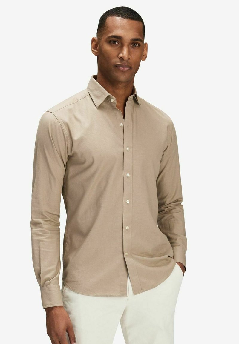 Ljusbrun långärmad skjorta med krage, med en knappfront och en slät yta. Bärs med vita byxor.