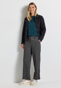Veste zippée bleu marine foncé sur un haut turquoise, associée à un pantalon large à carreaux gris et des baskets blanches, avec deux accents de boutons.