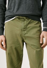 Pantalons en coton vert olive avec une taille à cordon de serrage, dotés d'une fermeture éclair à l'avant, de poches latérales et d'une texture lisse et légère.