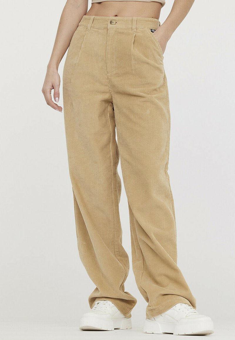 Pantalon en velours côtelé beige à jambes larges, doté d'une taille haute, de deux poches avant et d'une texture lisse. Associé à des baskets blanches à plateforme.