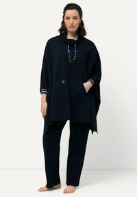 Tummansininen poncho hupulla, jossa on etutasku ja kontrastiväriset raidalliset hihansuut. Yhdistettynä samanvärisiin tummansinisiin housuihin, pehmeä kangaslaatu.