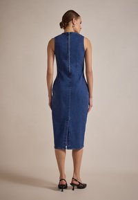 Rochie midi din denim de culoare albastru închis, fără mâneci, cu o siluetă ajustată. Are un fermoar la spate și o fente la tiv pentru ușurința mișcării.