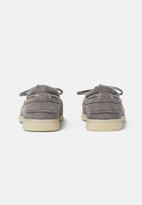 Zapatos de barco de ante gris con detalles de cordones, punta redondeada, textura suave y suela de goma crema contrastante. La vista trasera muestra detalles de costura.