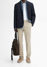 Blazer navy, camicia in denim azzurro chiaro, t-shirt bianca, pantaloni beige, borsa in camoscio marrone e scarpe color tan. Vestibilità su misura, linee pulite e colori neutri.