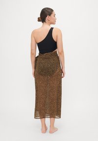 Maillot de bain noir à une épaule associé à une jupe enveloppante en tulle marron à motif léopard, avec une taille haute et une texture légère.
