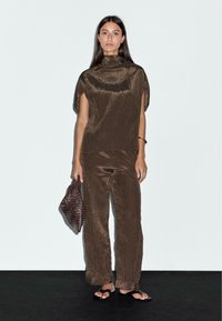 Maglietta a righe verticali marroni e pantaloni in maglia con maniche ampie e vestibilità comoda. Abbinata a una borsa con texture marrone scuro e sandali piatti.
