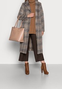Dlouhý kostkovaný kabát v šedé a hnědé, žebrovaný rolák v béžové, hnědé kostkované cropped kalhoty, béžová taška a hnědé kotníkové boty na podpatku.