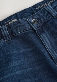 Jeans de mezclilla de corte relajado en azul oscuro. Presenta un clásico diseño de cinco bolsillos, cierre de botón metálico y un sutil desgastado en la tela.