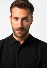 Zwarte poloshirt gemaakt van textuurstof, met een drie-knops sluiting en een reliëflogo op de linkerborst. Eenvoudig en klassiek ontwerp.