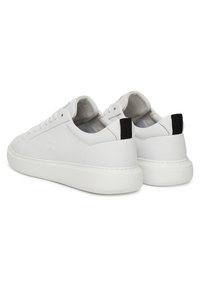 Balti sporta apavi ar gludu ādas materiālu, apaļu formu un baltu zoli. Melns akcents papēdī un minimālistisks dizains.