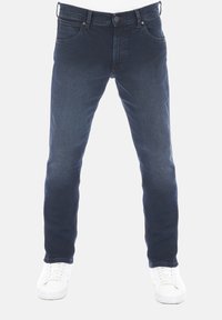 Jeans de mezclilla azul oscuro con un corte ajustado, cinco bolsillos y costuras en contraste, combinados con zapatillas blancas sobre un fondo plano.