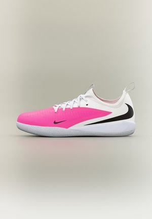 Chaussure de soccer d'intérieur basse avec l'avant rose, l'arrière blanc, des logos Nike Swoosh noirs, des lacets blancs et une semelle texturée grise.