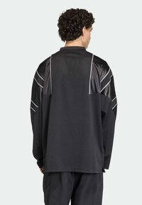 Crna atletska majica s dugim rukavima, mrežastom teksturom i sjajnim panelima; ima bijele obrube i opušteni kroj.